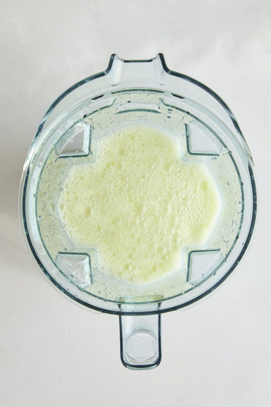 Top-down view of a blender pitcher filled with Brazilian Lemonade - a light green, frothy liquid, set against a plain white background.