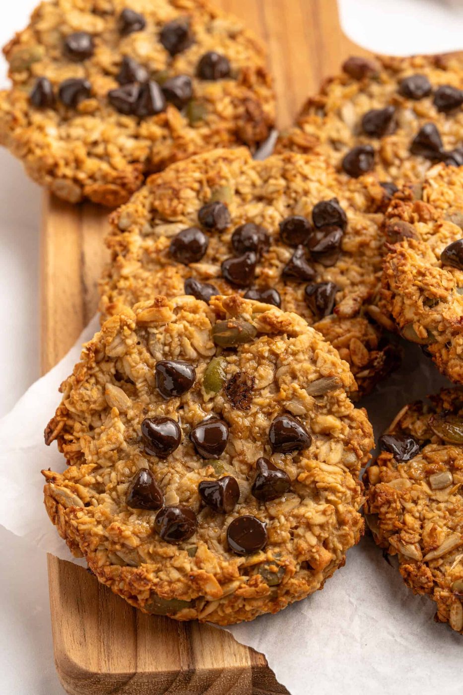 Close-up of several freshly baked Breakfast Cookies, featuring visible oats and scattered chocolate chips on top, arranged on a wooden board. The cookies appear golden brown and perfect for a morning treat.
