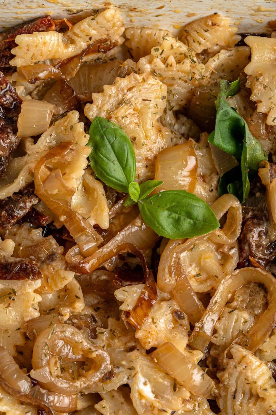 Close-up of bow-tie pasta mixture garnished with fresh basil leaves. The dish appears creamy and seasoned with herbs.