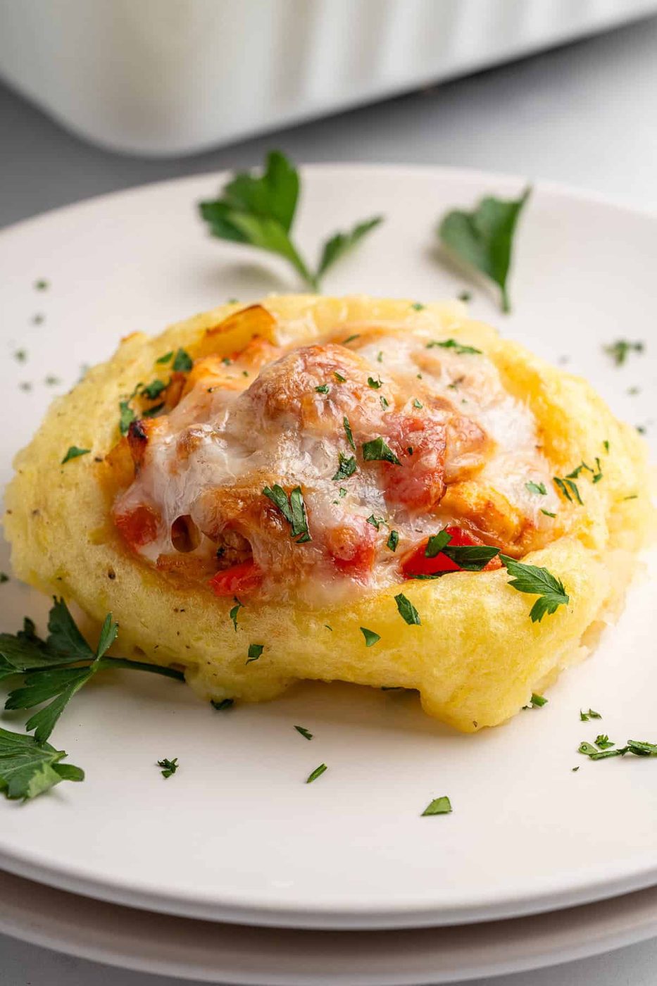 A close up of a chicken mashed potato nest, golden brown, filled with the cooked chicken and vegetable mixture and topped with melted cheese. Garnish of chopped parsley on top and around the dish. 