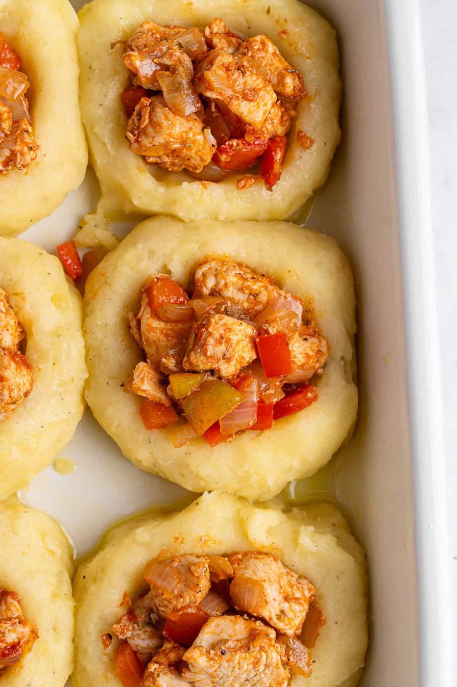 A close up of a mashed potato nest filled with a scoop of cooked chicken and vegetable mixture. 