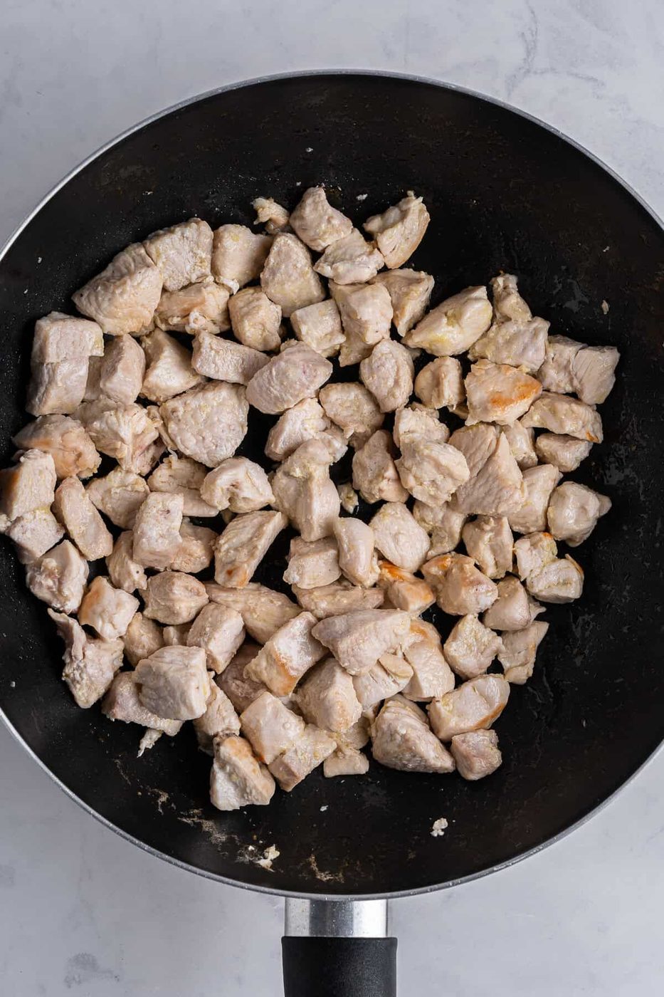 A saute pan of cubed pieces of chicken cooking.