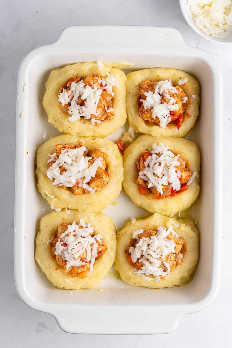 A baking dish with six mashed potato nests filled with a chicken cubes and vegetable mixture and topped with grated cheese. 