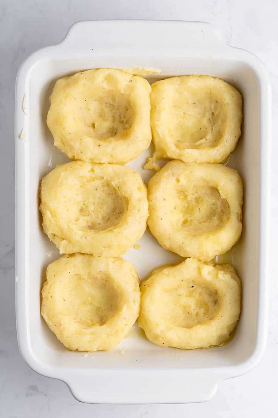 A casserole dish with 6 mashed potato nests. 