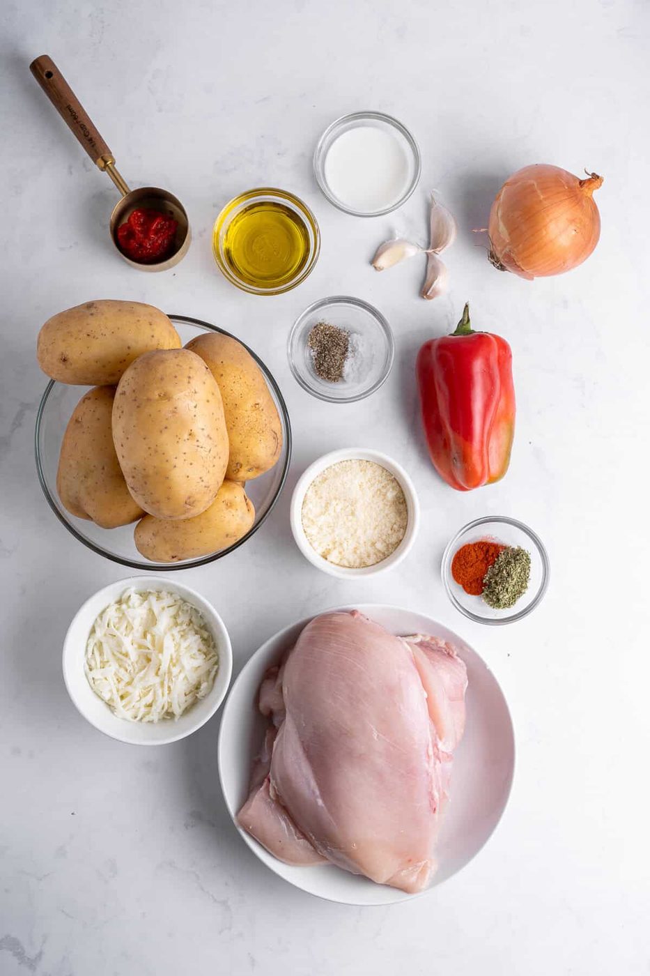 a flat lay of ingredients for the chicken mashed potato nests. Ingredients include potatoes, cheese, chicken breasts, a pepper, various spices and olive oil. 