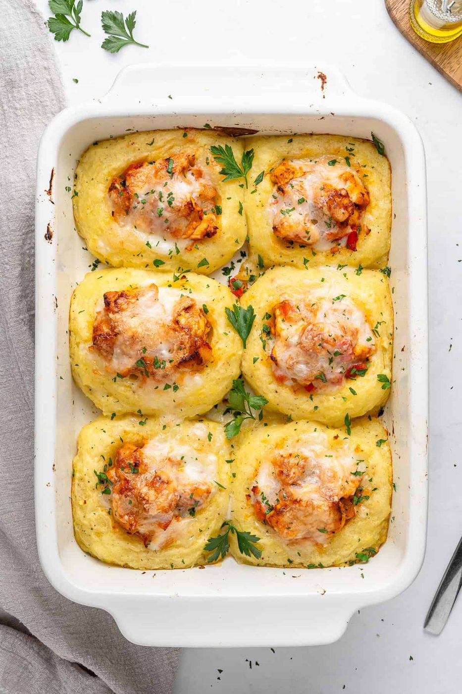 A casserole dish with six baked and golden Chicken mashed potato nests topped with melted cheese and garnished with chopped parsley. 