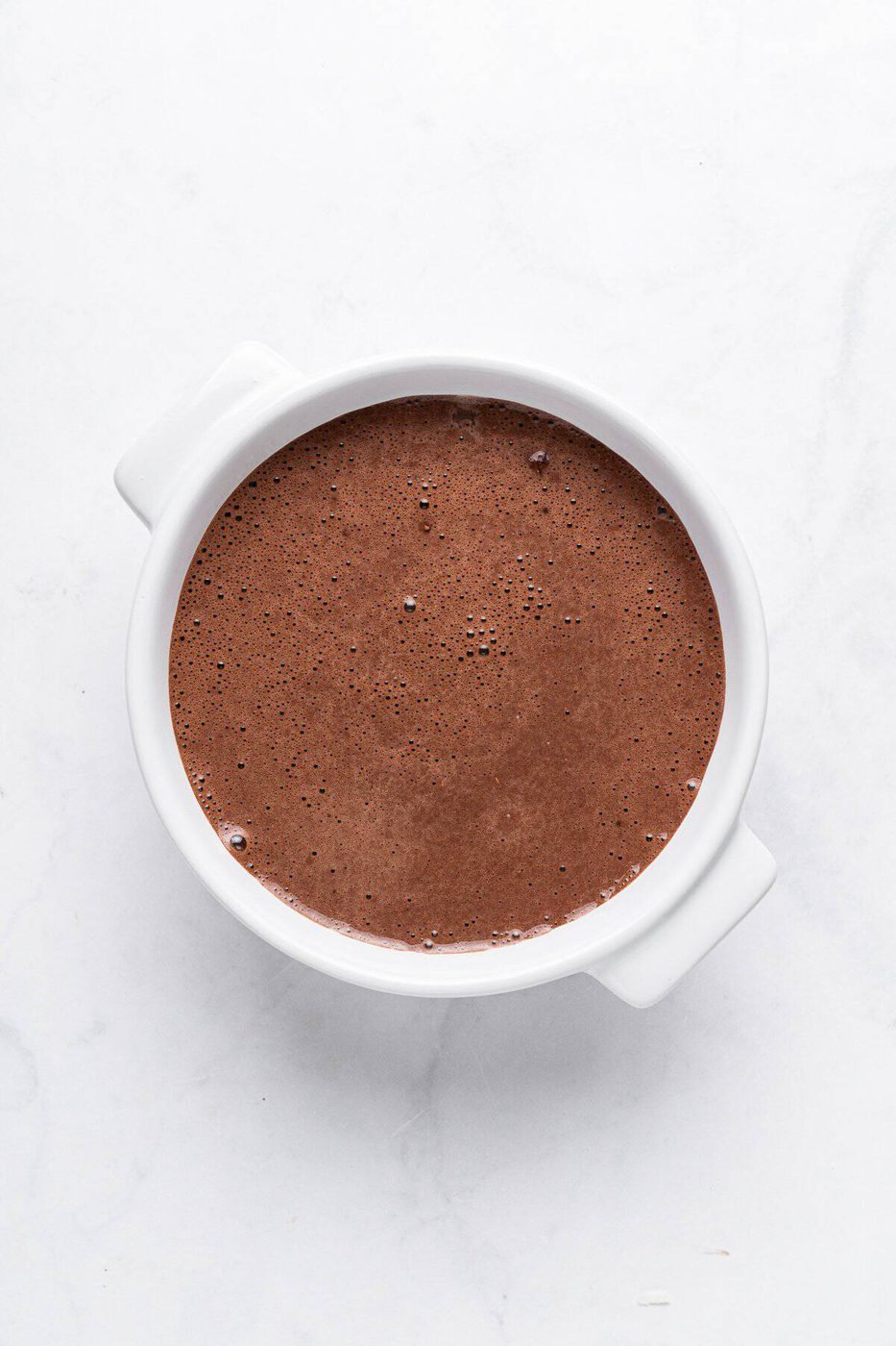 A white ceramic bowl filled with smooth, rich chocolate batter on a light marble surface.