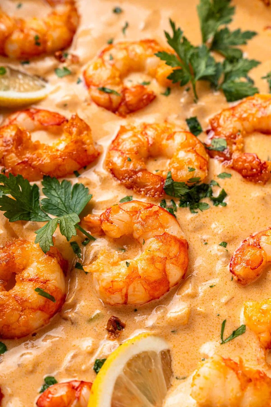 Close-up of creamy garlic butter shrimp garnished with fresh parsley and lemon slices. The golden-brown shrimp are coated in a rich, velvety sauce, creating a mouthwatering dish.