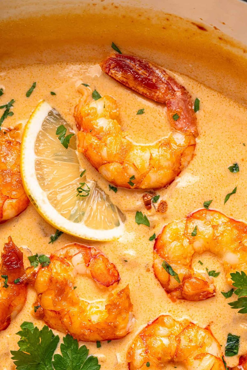 Creamy shrimp dish garnished with fresh herbs and a lemon wedge. The shrimp are cooked in a rich, orangish sauce, with visible herbs sprinkled on top, creating an appetizing and vibrant presentation.
