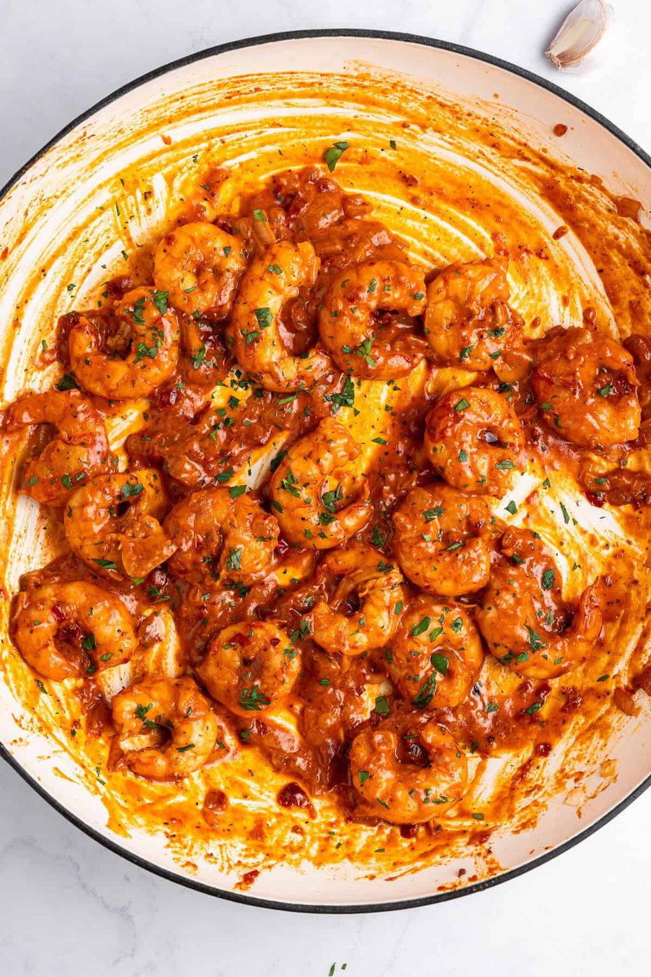 A skillet filled with cooked Creamy Tuscan shrimp in a rich, tomato-based sauce garnished with chopped herbs. The sauce has an orange-red hue, coating the shrimp thoroughly. The dish appears flavorful and spicy.