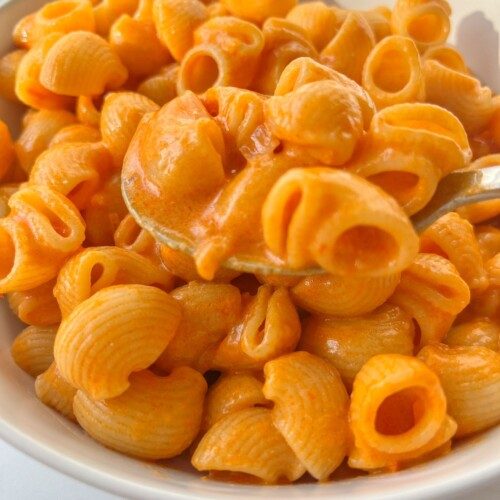 A close-up of a bowl of pasta shells coated in a creamy orange sauce, with a spoon lifting some pasta from the bowl—just like the famous Copycat Carbone Spicy Rigatoni.