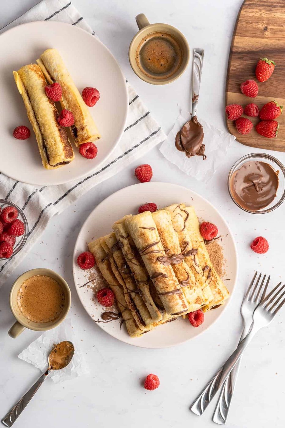 a beautiful table with cutlery, raspberries for garnish and French toast rolls that are plated 