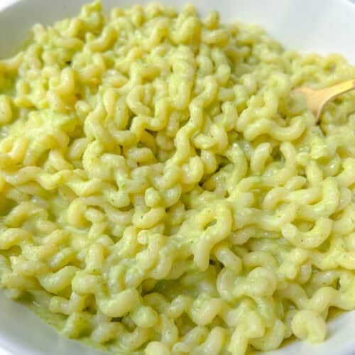 A close-up of a bowl filled with creamy, green Broccoli Ricotta Pasta, likely coated in a pesto or avocado sauce, with a fork partially visible on the right side.