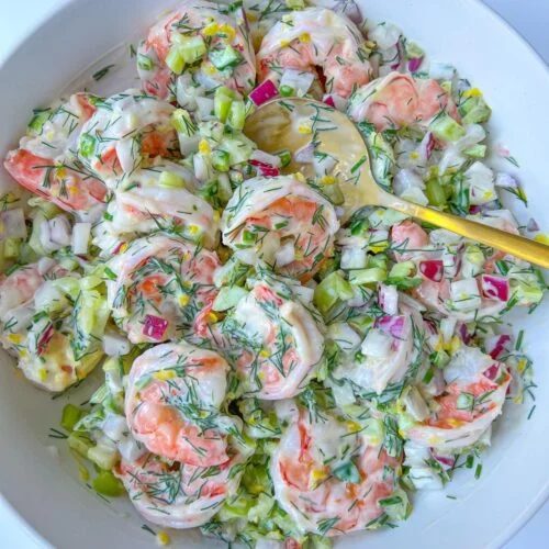 A bowl of Creamy Shrimp Salad with chopped celery, red onion, and fresh dill, all mixed together and served with a yellow serving spoon.