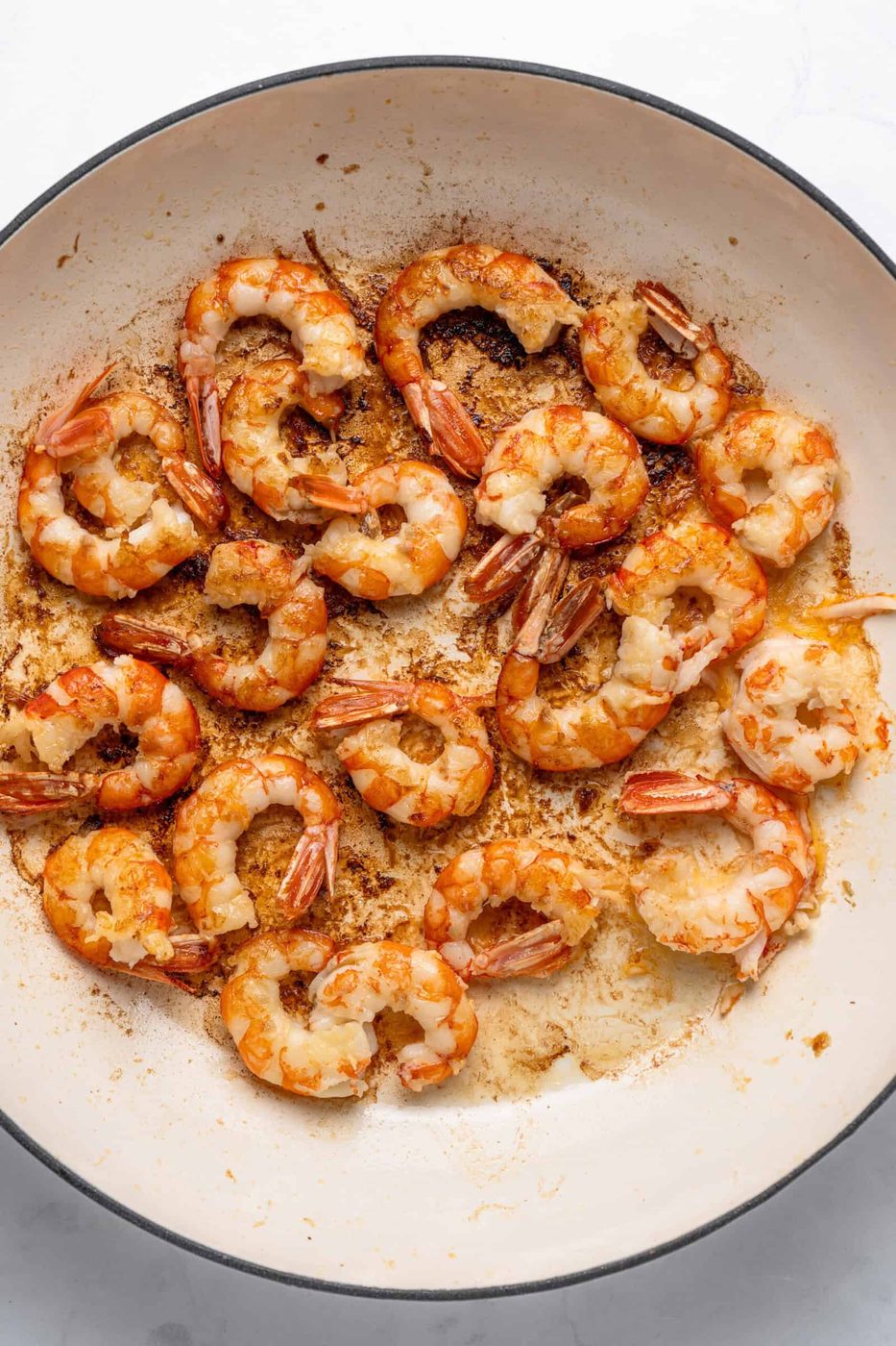Cooked shrimp in a large white pan, seasoned and arranged in a circular pattern. The shrimp are slightly browned, indicating they were sautéed, with visible oil and spices on the pan.
