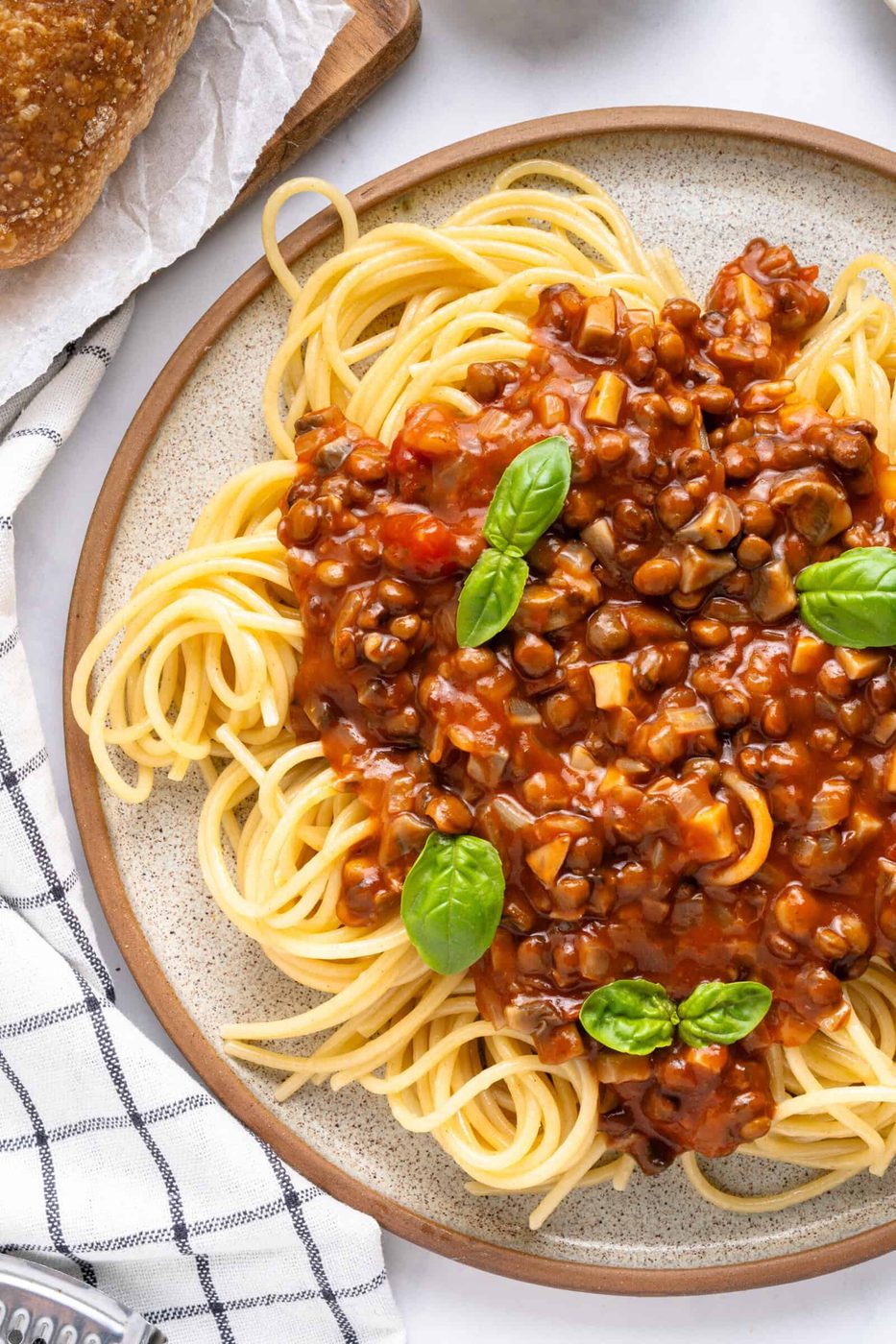 A plate with spaghetti, lentil bolognese and basil on top.