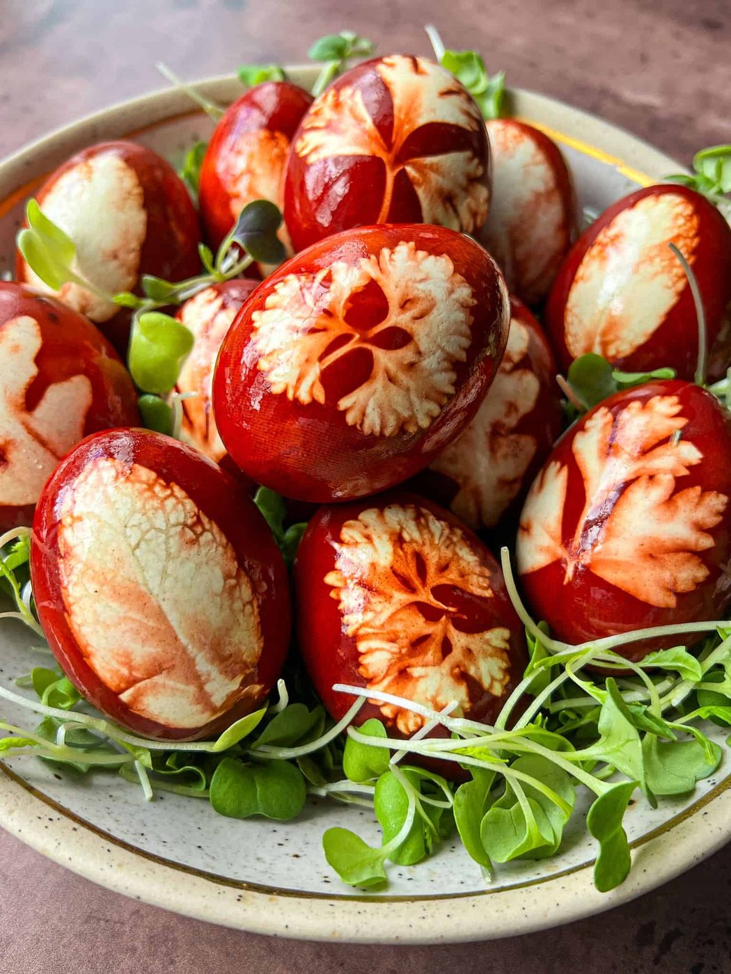 A bowl of red-brown eggs featuring intricate leaf patterns, nestled on a bed of fresh green sprouts. The eggs have a marbled appearance, showcasing a variety of natural textures.