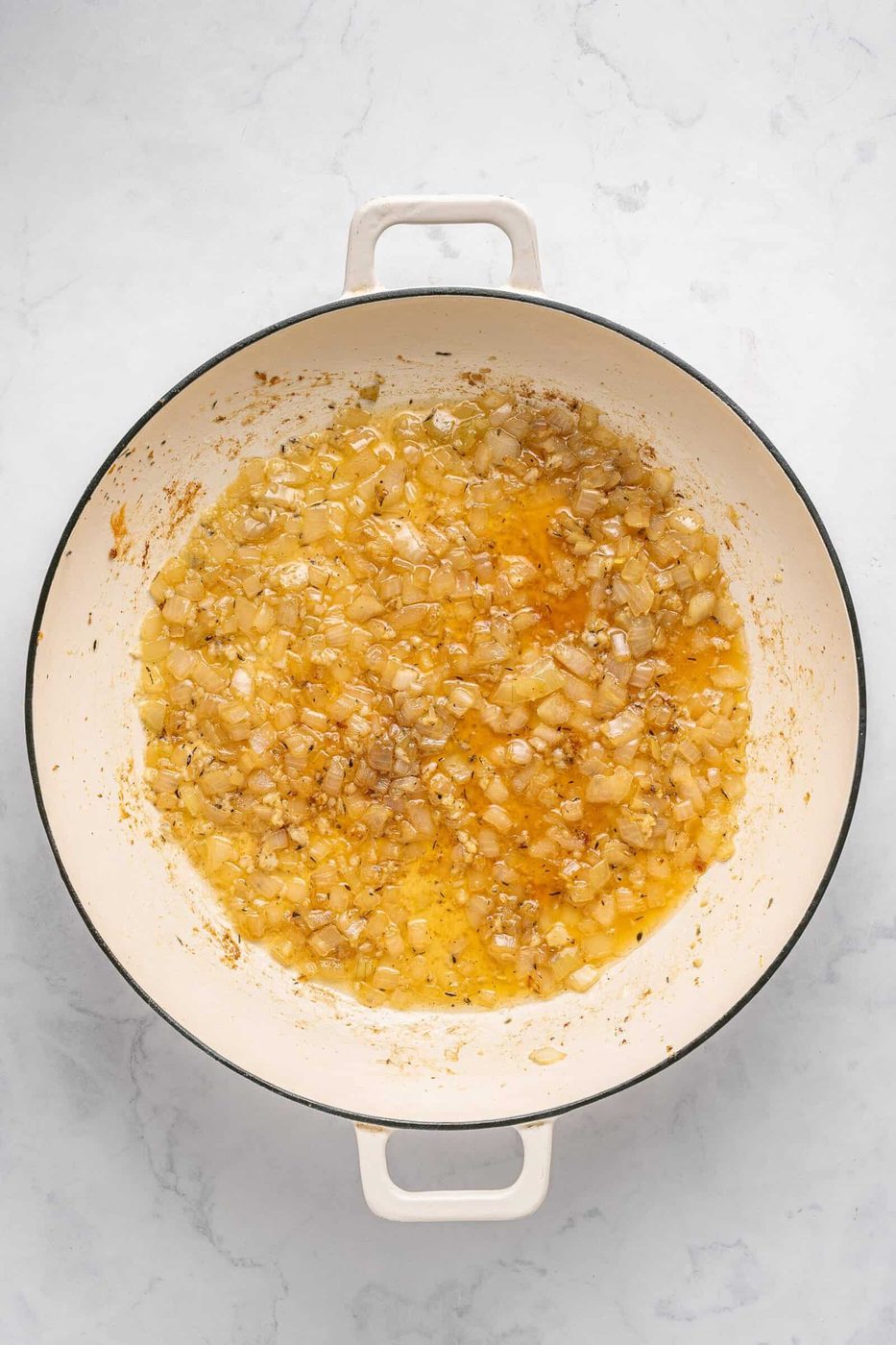 Diced onions sautéing in oil in a large white enameled pot on a light marble countertop, creating the flavorful base for an easy One Pan Chicken Dinner.