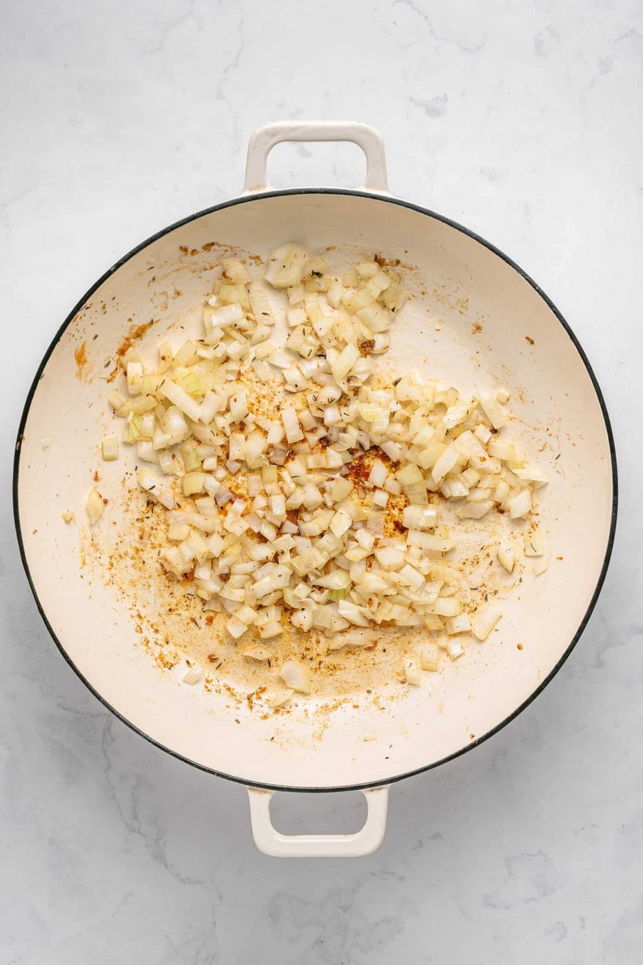 Chopped onions sautéing in a large white enameled skillet, developing browning and caramelization—the perfect flavorful base for a one pan chicken dinner.