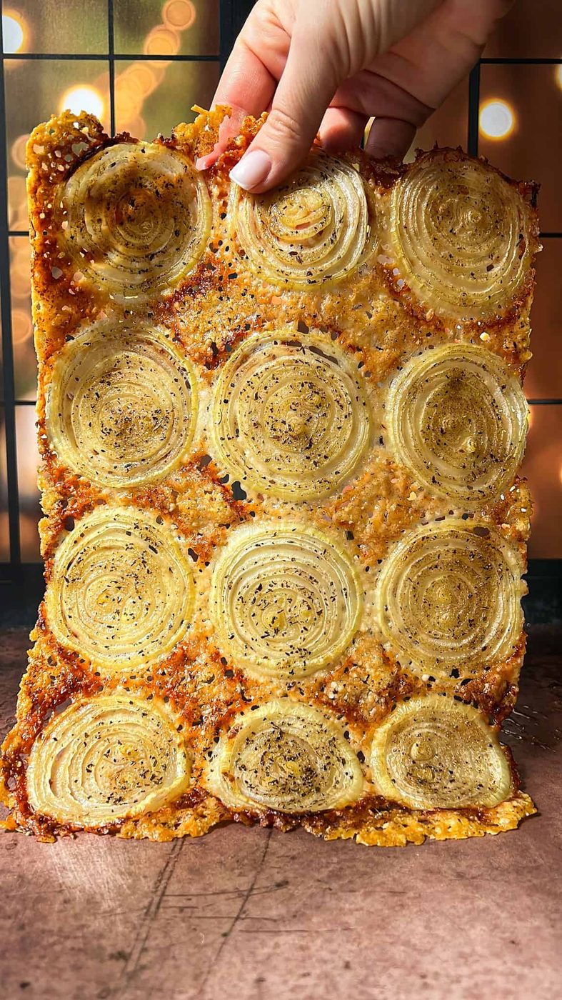 The edges are golden brown, and visible seasoning includes black pepper. A soft-focus background with warm, glowing lights adds a cozy ambiance.