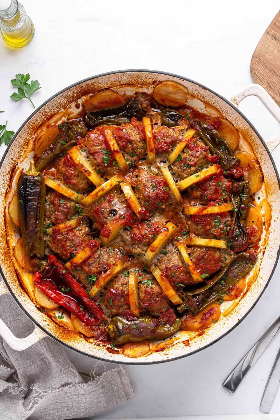A round baking dish filled with baked vegetables, arranged in a star pattern. Includes tomatoes, potatoes, and peppers, topped with herbs. The dish is on a white surface with a napkin and a fork nearby.