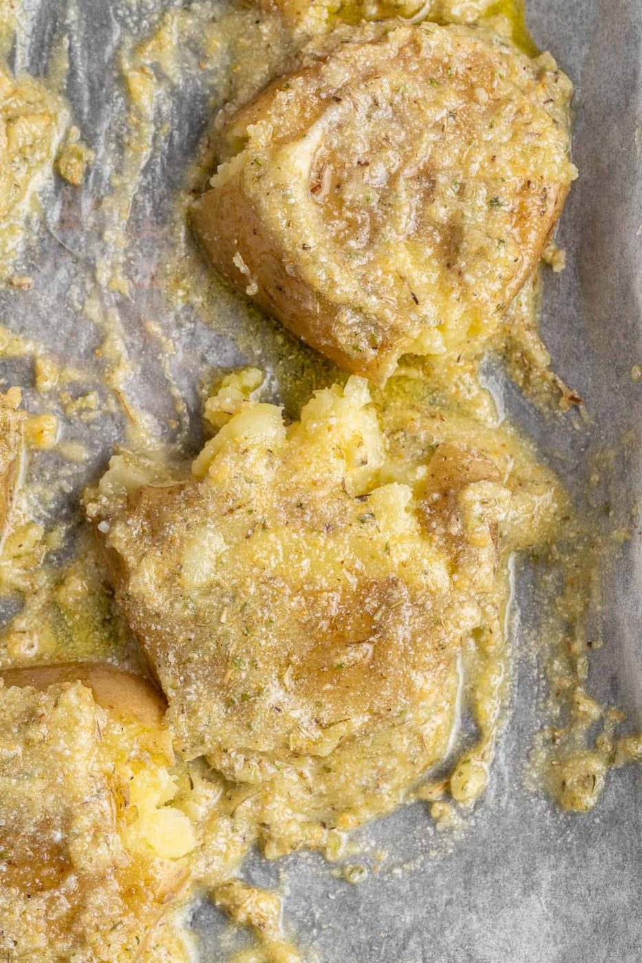 Close-up of entree topped with melted cheese on a parchment-lined baking sheet. The golden cheese is slightly crusted, covering the mashed pieces, and the surface is dotted with specks of seasoning.