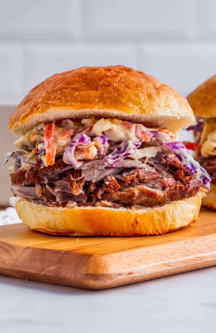Pulled pork sandwich with coleslaw on a wooden board. The sandwich features tender, shredded pork topped with creamy coleslaw in a soft, golden bun.