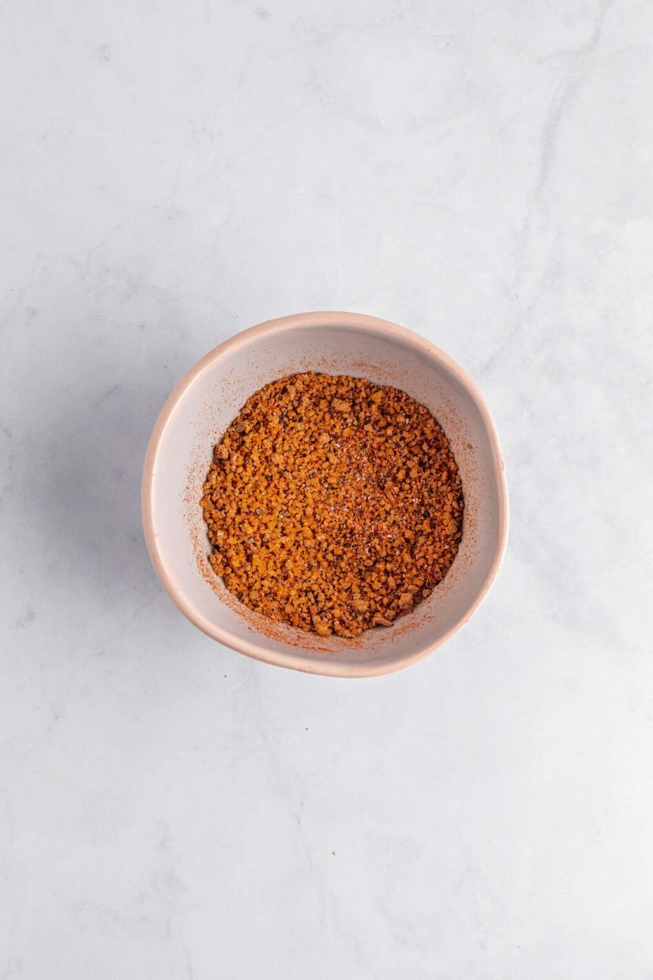 A bowl filled with a finely ground reddish-brown spice mixture, placed on a white marble surface.