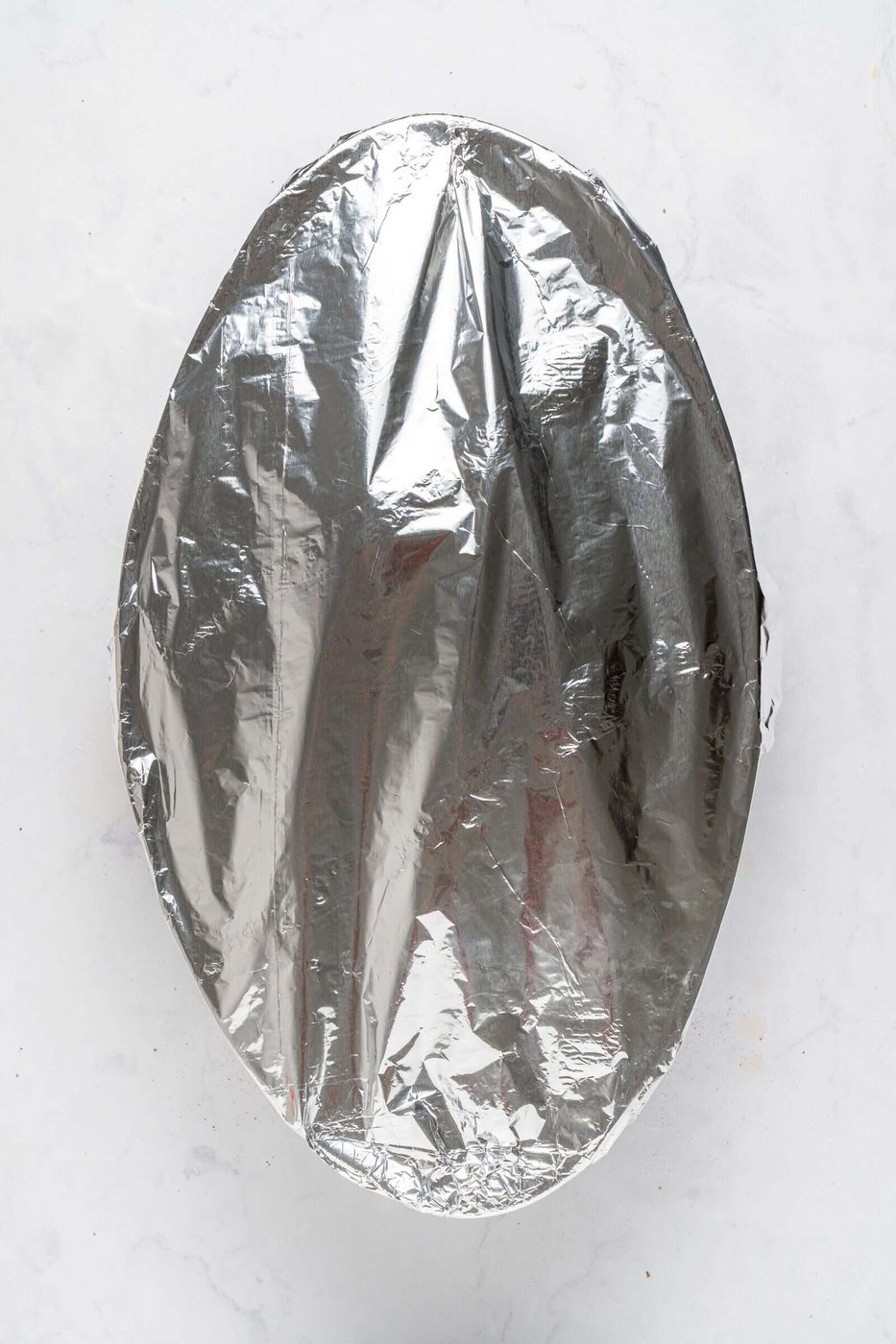 A round dish covered with shiny aluminum foil on a light, textured surface.