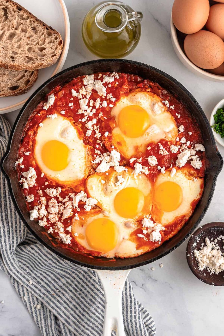 A skillet with sauce, eggs, and feta on top.