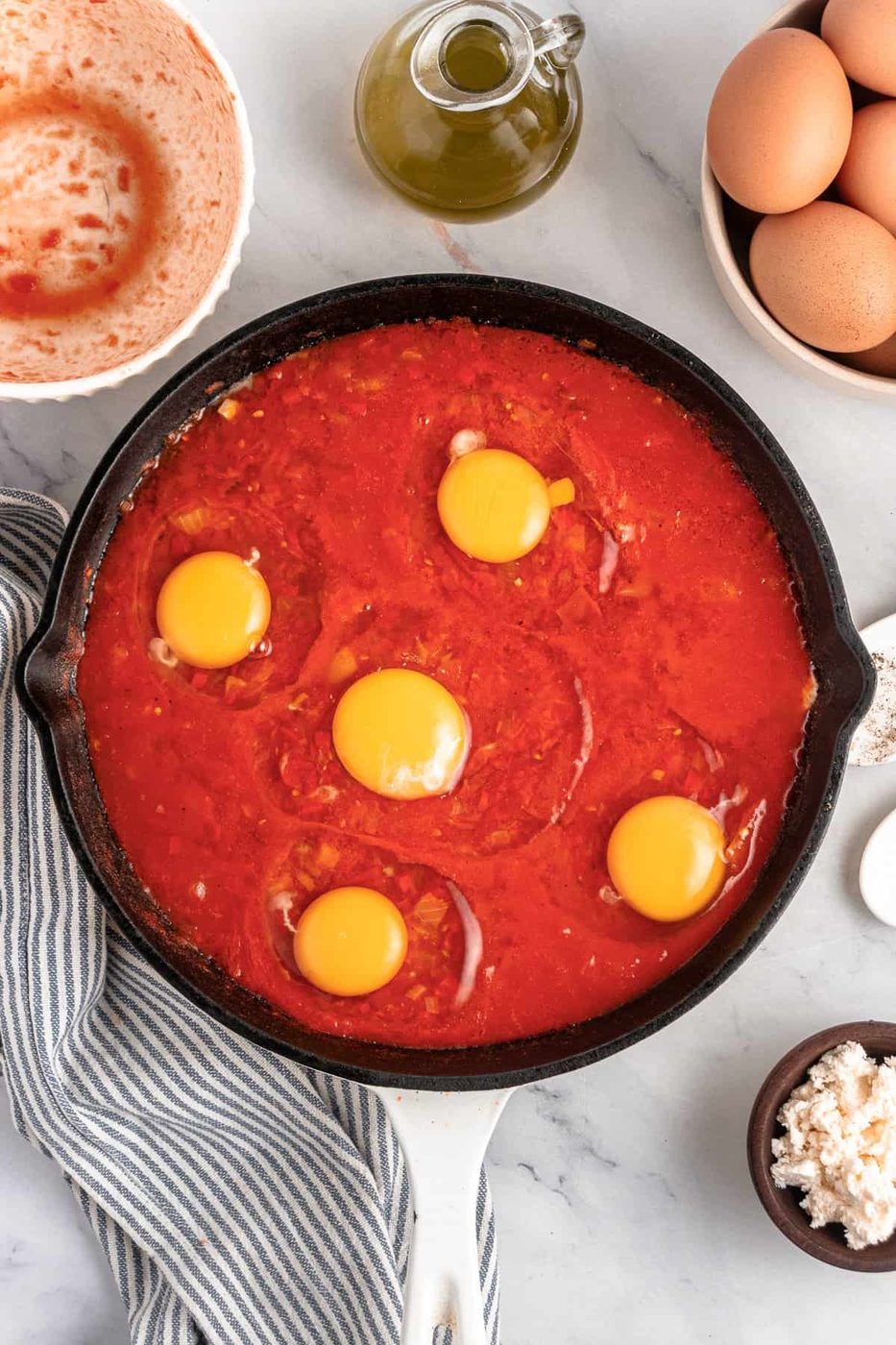 A skillet with cracked eggs on top of the tomato sauce.