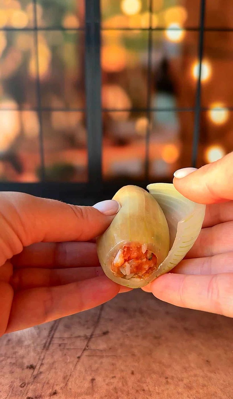 Two hands are peeling open a large cooked shell to reveal a red and orange filling against a blurred background with warm lighting.