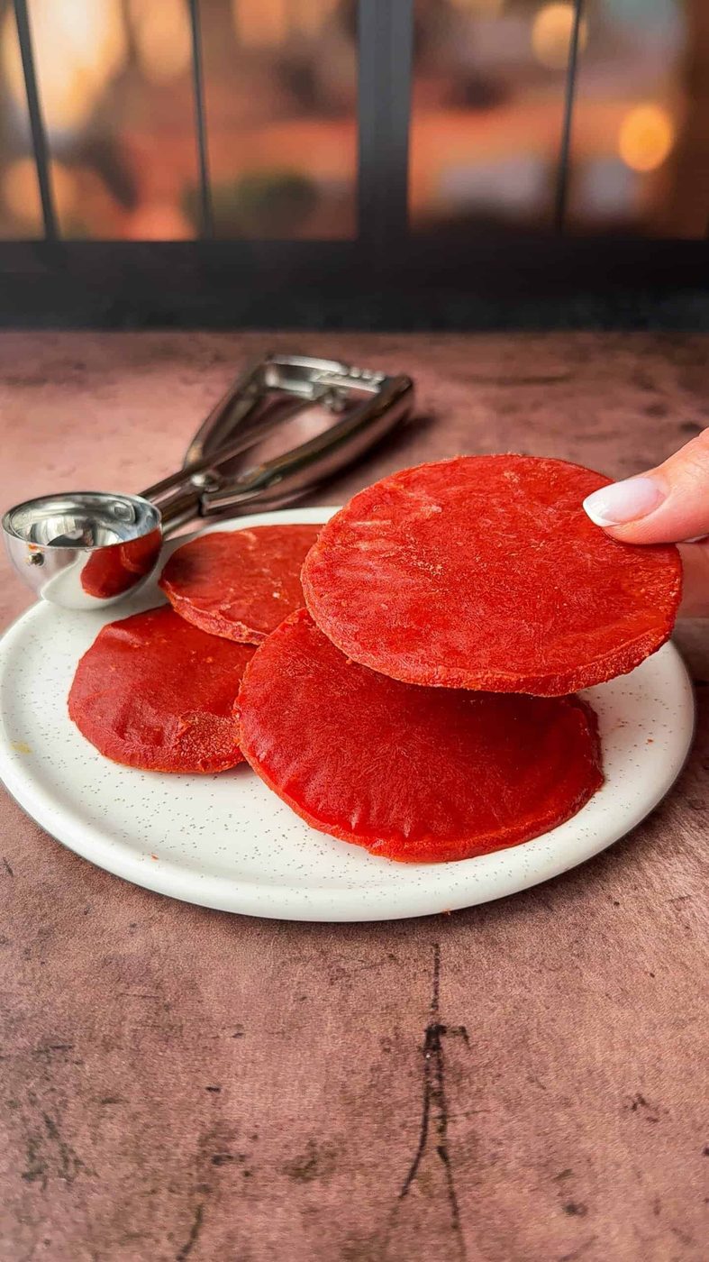 Close-up of a hand holding the red tomato paste circle above a white plate.