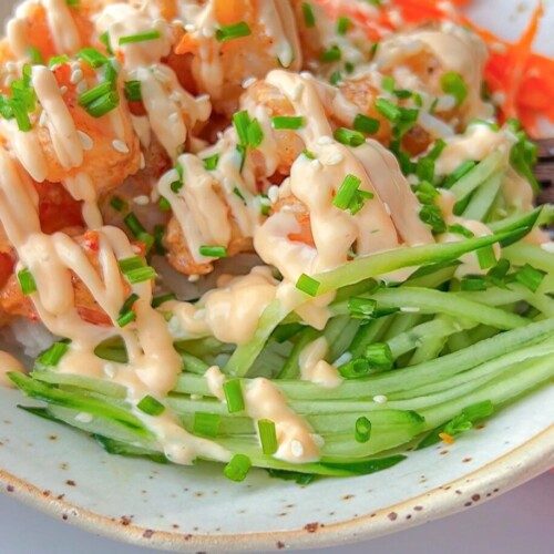 A bowl filled with crispy tofu cubes, shredded carrots, and julienned cucumber, topped with a creamy sauce and chopped chives.