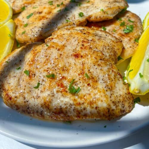 Grilled Lemon Chicken breasts garnished with chopped herbs, served on a white plate with lemon wedges on the side.