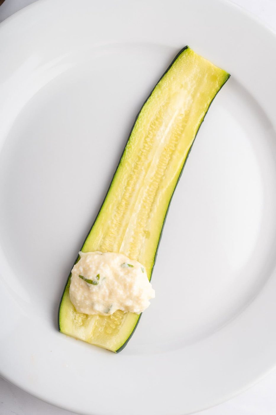 One slice of zucchini on a plate with the filling on one end