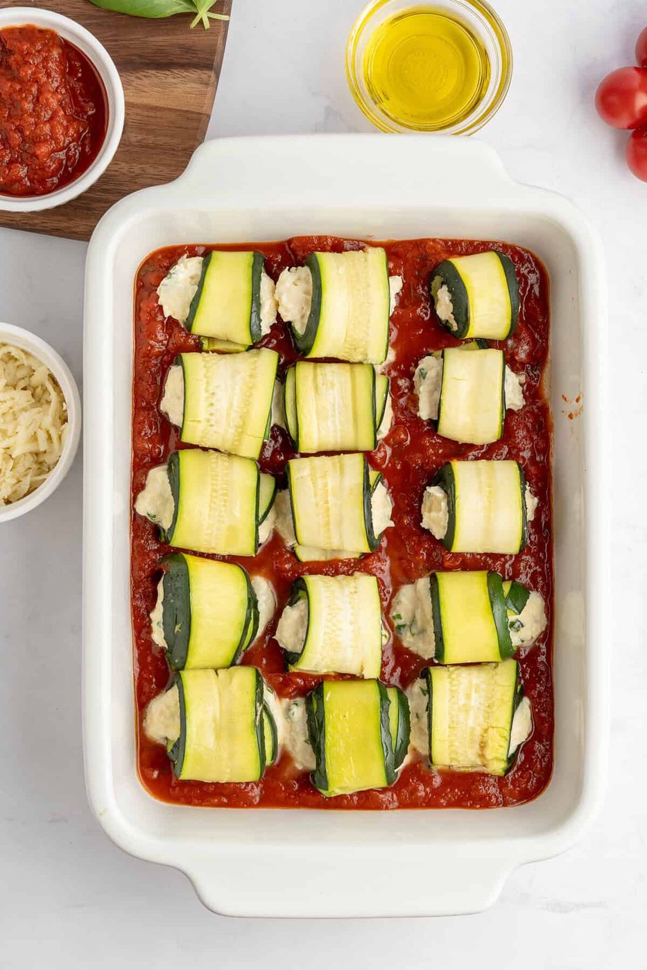 Marinara sauce in a baking dish with rolled up zucchini rolls in it 