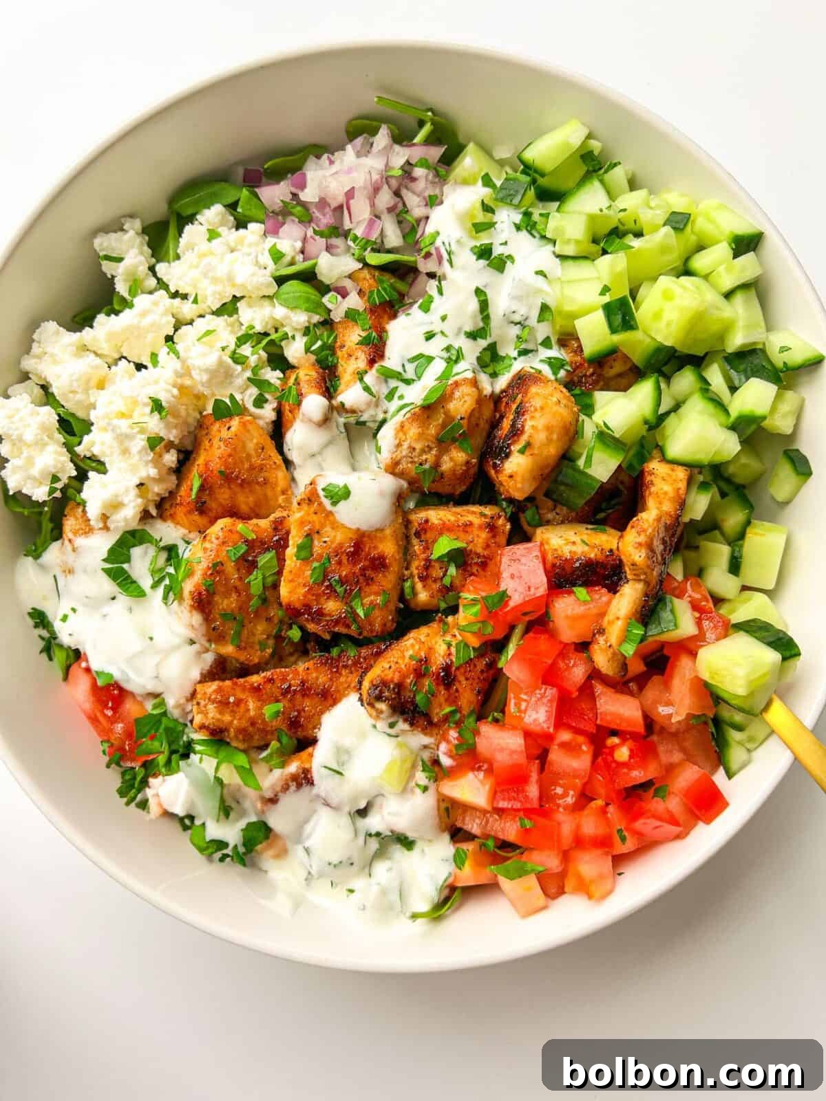A vibrant and fresh Easy Greek Bowl featuring perfectly grilled chicken, fluffy rice, crisp cucumbers, juicy tomatoes, red onions, briny Kalamata olives, and creamy feta cheese, all drizzled with a rich tzatziki sauce and garnished with fresh parsley.