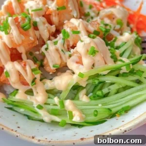 A bowl filled with crispy tofu cubes, shredded carrots, and julienned cucumber, topped with a creamy sauce and chopped chives.