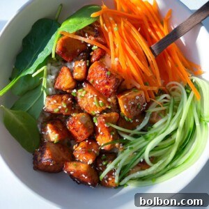 A vibrant bowl inspired by a Honey Garlic Salmon Bowl, featuring glazed tofu cubes, shredded carrots, spiralized cucumber, fresh spinach, rice, and a sprinkle of sesame seeds, served with chopsticks.
