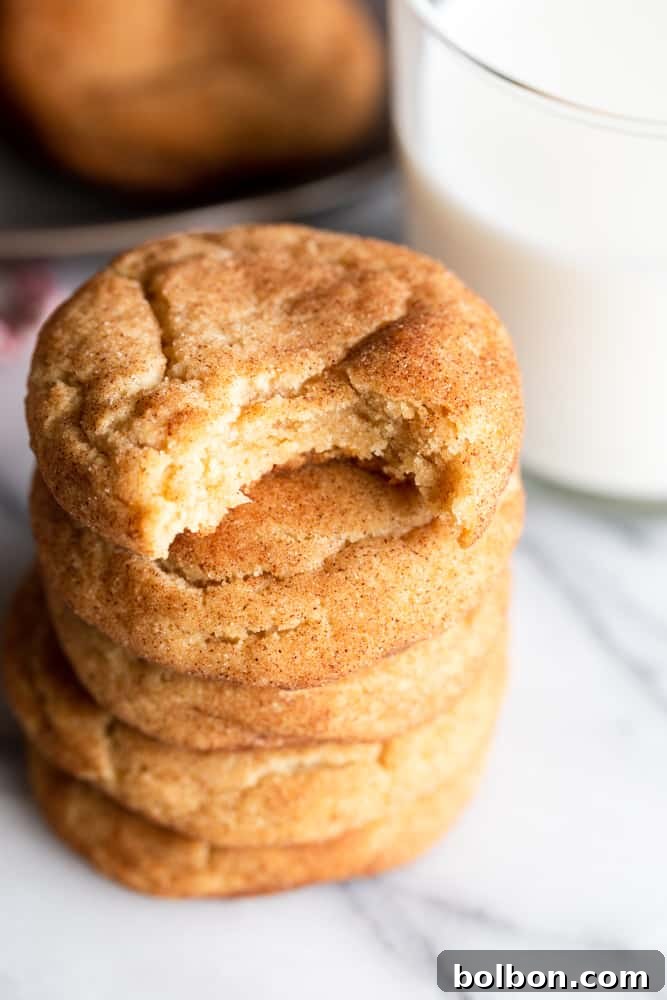 A close-up stack of five brown butter snickerdoodle cookies, with one cookie having a bite taken out, revealing its soft, chewy interior.