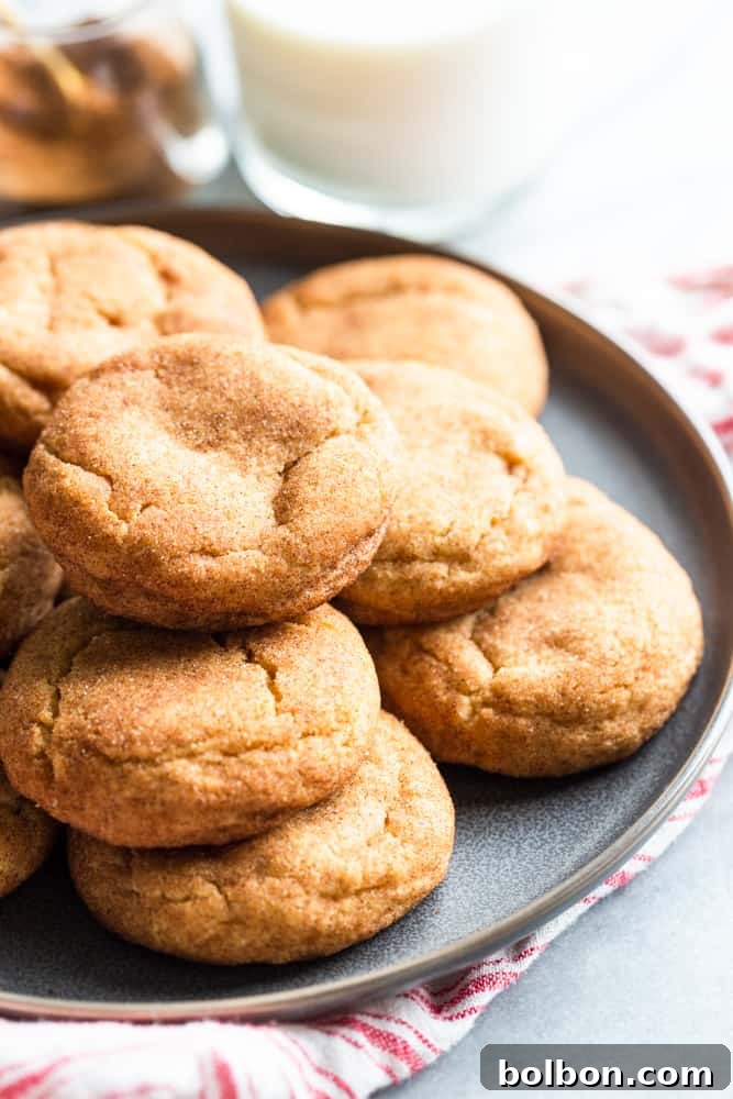 A cozy scene with a pile of golden brown butter snickerdoodles on a white plate next to a tall glass of milk, perfect for a treat.