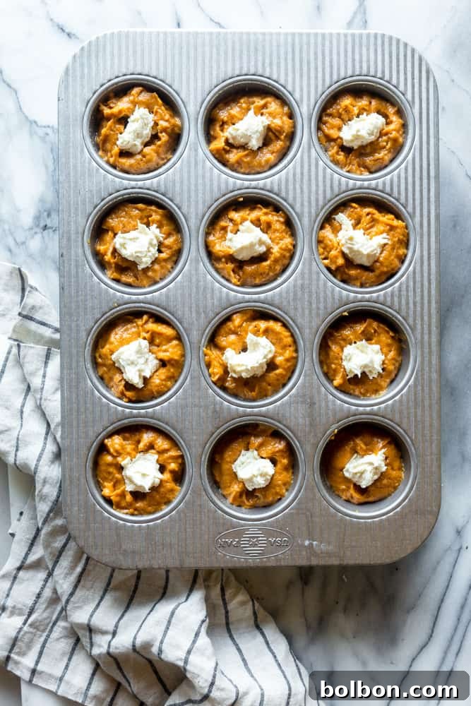 Pumpkin muffin batter with generous cream cheese dollops on top before baking, promising a rich swirl