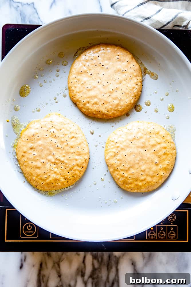 Several pumpkin pancakes cooking on a hot frying pan, showing bubbles forming on the uncooked side.