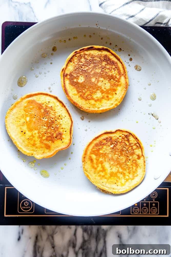 A stack of perfectly cooked golden-brown pumpkin pancakes resting on a white frying pan.