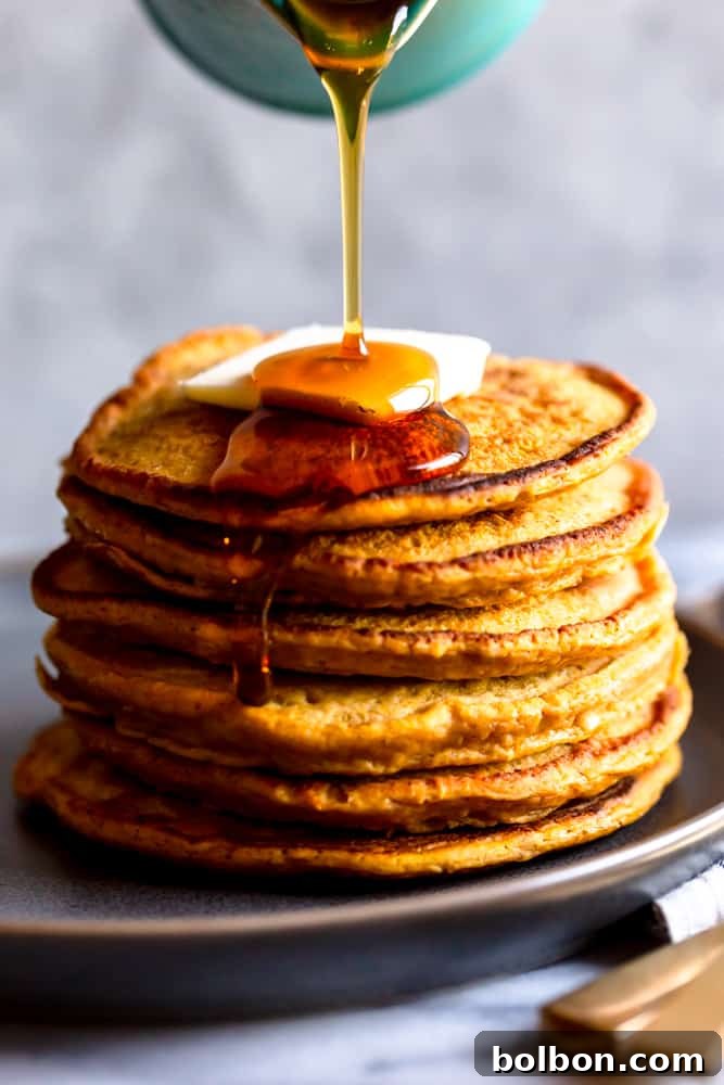Golden pumpkin pancakes stacked high with a generous drizzle of maple syrup cascading down the sides.