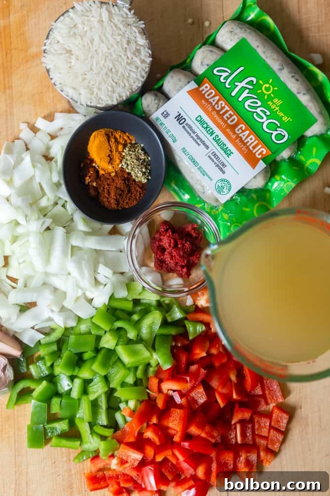 Chopped peppers, onions, chicken stock, rice, spices, tomato paste, and chicken sausage on a cutting board, ready for the One-Pot Sausage and Rice Skillet