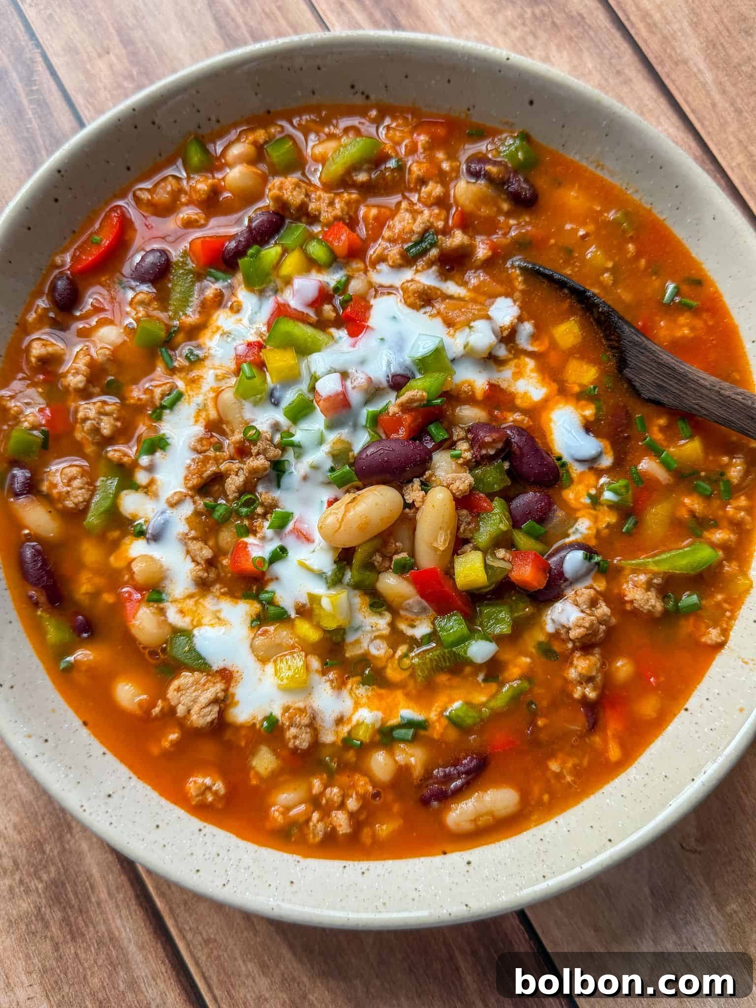 Guilt-Free Turkey Chili 2 A vibrant bowl of healthy turkey chili, garnished with fresh sour cream, chopped chives, and a sprinkle of red bell pepper, highlighting the rich texture of ground turkey, kidney beans, and white beans.