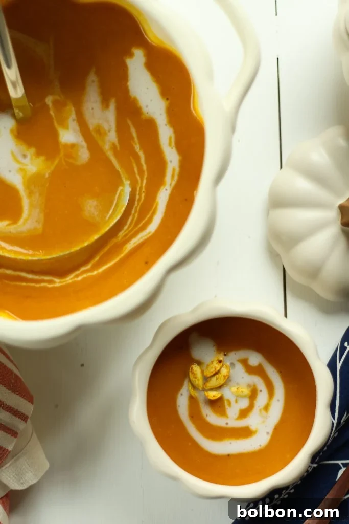 A top-down view of a vibrant orange Roasted Pumpkin Coconut Curry Soup in a white bowl, garnished with a swirl of coconut milk and crunchy roasted pumpkin seeds.