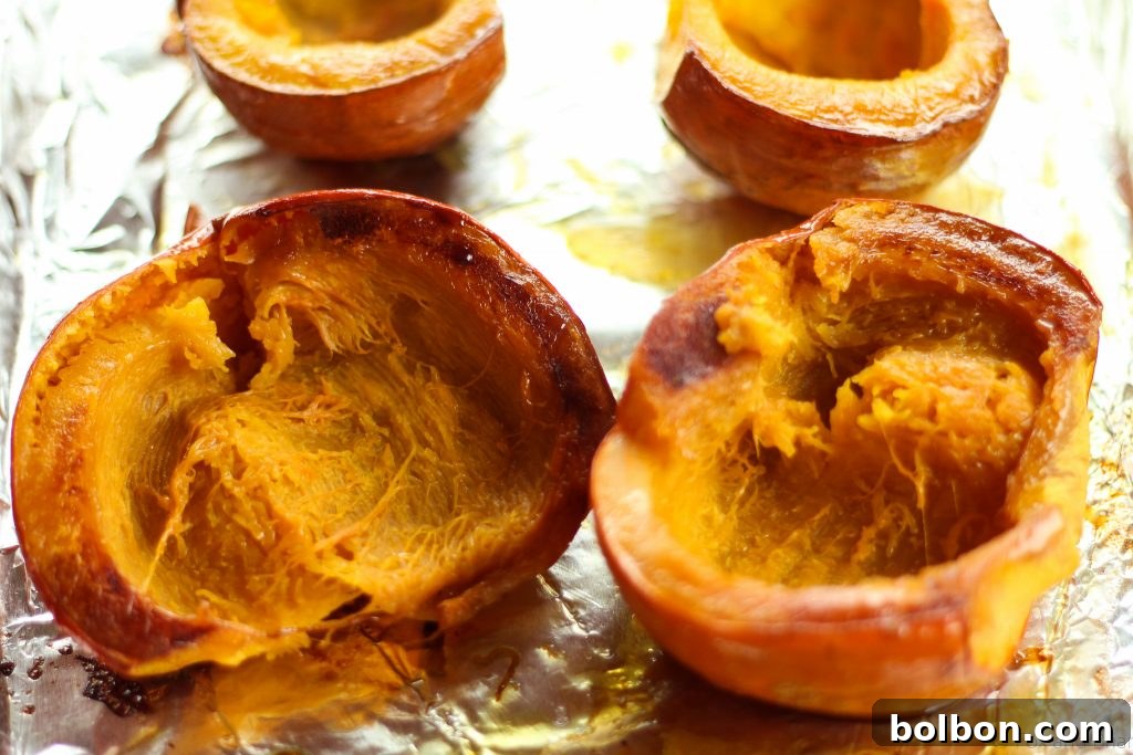 Scooping out the soft, cooked pumpkin flesh from its skin after roasting, revealing the smooth texture.